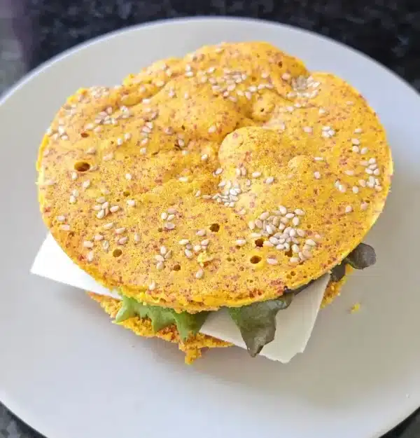 Pão sem glúten com cúrcuma e sésamo, recheado com folhas verdes, num prato branco